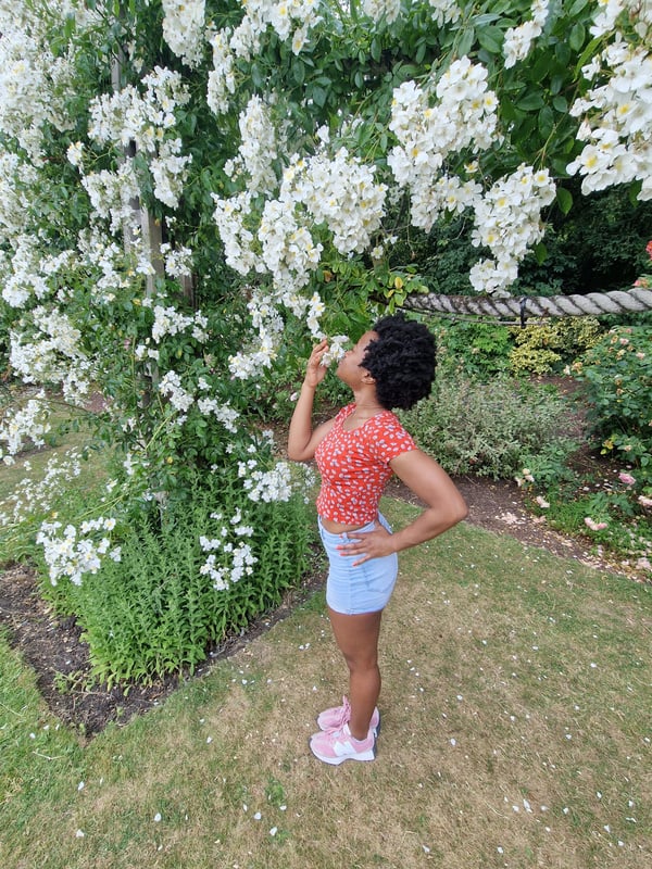 A slim woman standing in front of a tree, smelling white flowers